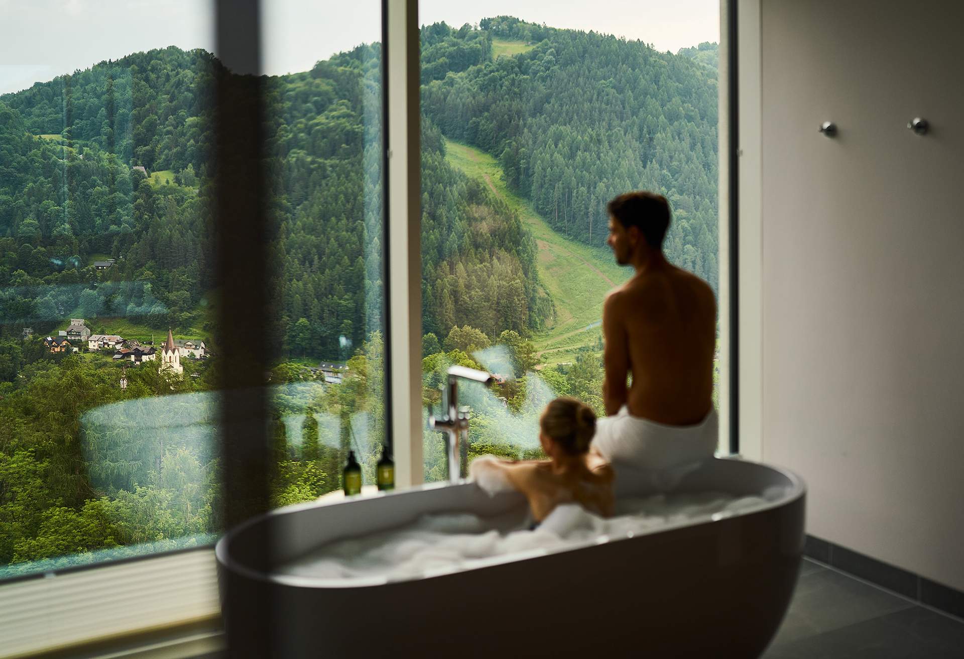 Couple relaxing in spa bathtub by a window with view over a valley, Poland